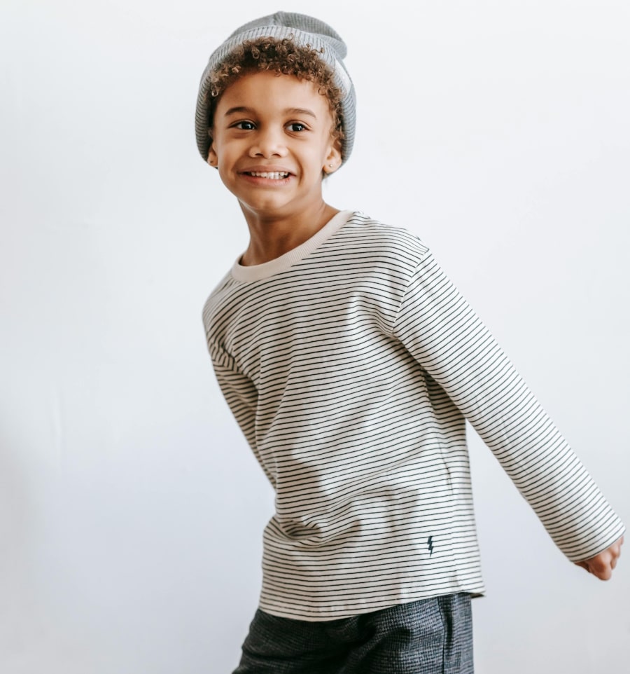 Boy wearing a striped sweater and dark pants on a plain background